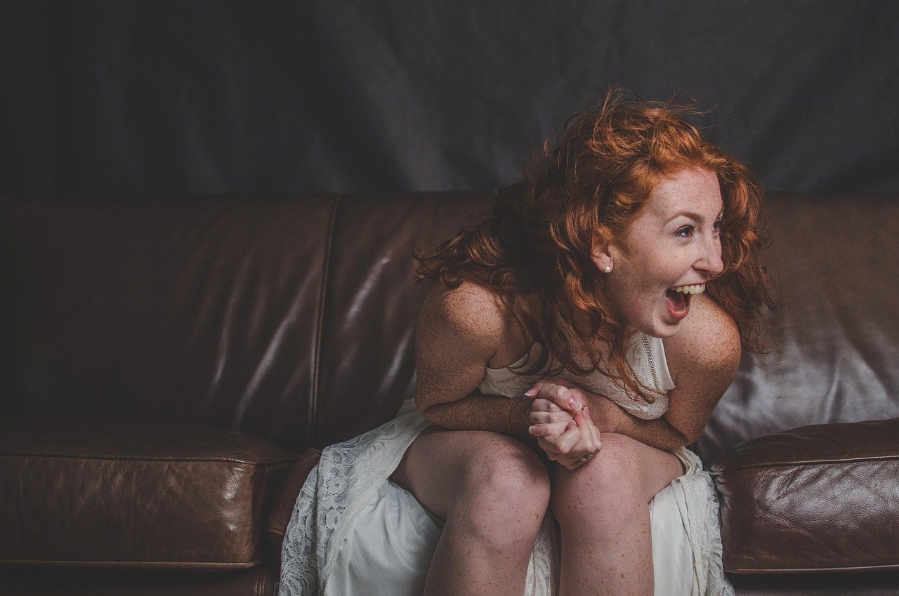 Red-haired woman laughing on a leather sofa